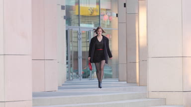 Fashion model in black with red bag walking towards the camera