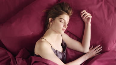Beautiful woman waking up in her bedroom in red bad linen