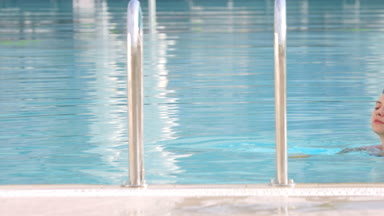 Girl in blue swimwear exit the swimming pool by ladder