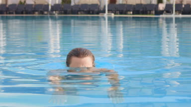 Young attractive girl in swimming pool dive and pops up