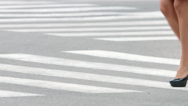 Young slim woman on high heels walking along the pedestrian crossing