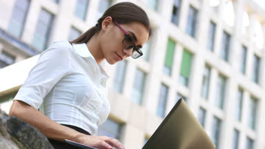 Business woman chatting online via laptop against business building