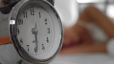 Beautiful woman waking up in the morning by alarm clock