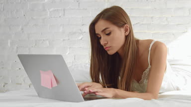 Young attractive woman lying in bed and working on laptop
