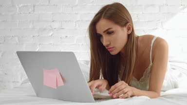 Young attractive woman in sleepwear lies in bed and use laptop