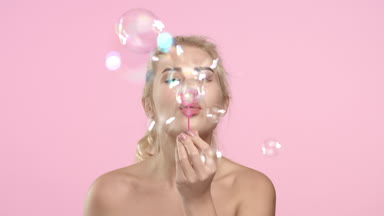 Young positive woman blowing soap bubbles and smiling.