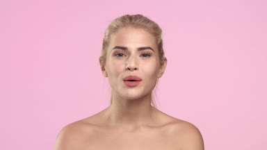Young woman on light pink background blowing in the camera