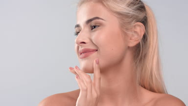 Blonde woman gently strokes her smooth face skin