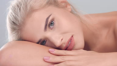 Blonde woman lay head on her hand and strokes her smooth skin