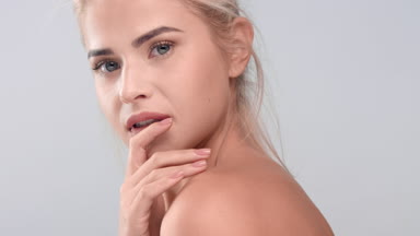 Woman gently touches her bare shoulders and looks at the camera