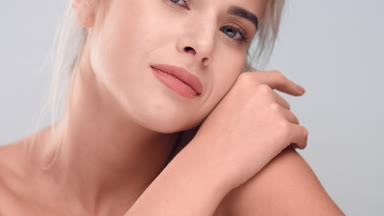 Woman looks at the camera, smiles and softly touches her neck