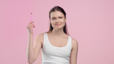 Woman throws out razor and smiling on light pink background