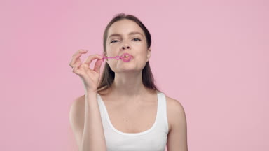 Young woman blowing bubbles against a light pink background