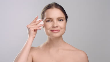 Young woman demonstrates usage of cotton pad and smiling