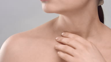 Woman gently strokes her clavicles on light grey background