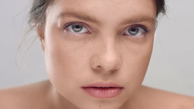 Woman, softly touches face skin, looks at the camera and smiles