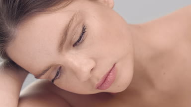 Woman looks up at the camera, touching her face and smiling