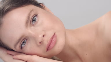 Woman raises her head, looks at the camera touches her face.