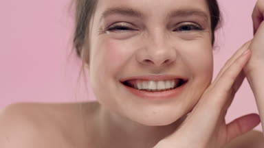 Young wide smiling woman looks at the camera on pink background