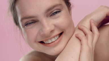Young smiling woman looks at the camera on pink background
