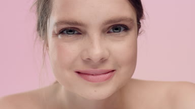 Young freckled woman looking at camera and smiling on pink bg