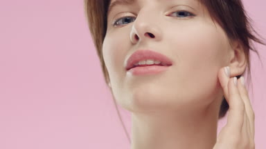 Brunette woman with smooth healthy skin gently strokes her face