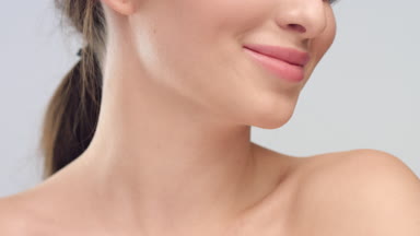 Young woman with smooth healthy skin smiles on grey background
