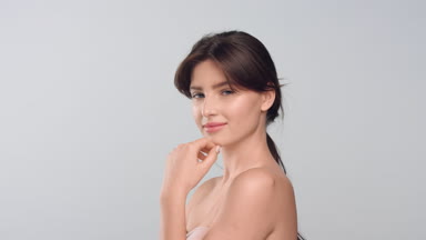 Woman with smooth skin touches her face, looks at camera and smiles