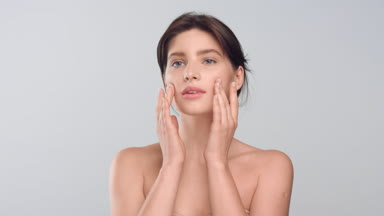 Young woman with elastic skin gently touches her face and smiles