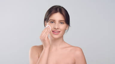 Young woman with healthy skin using cotton pad and smiling