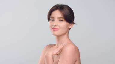 Young brown-haired woman gently touches her face and neck