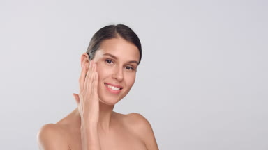 Young slim woman with smooth skin touches her face and smiles