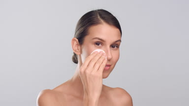Young positive woman with smooth skin uses cotton pad and smiles
