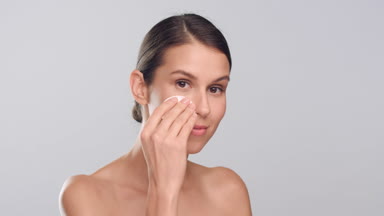 Young slim woman with healthy skin uses cotton pad and smiles