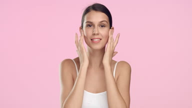 Young slim woman gently strokes her face with hands and smiles