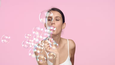 Young slim brunette woman blows soap bubbles and smiles.