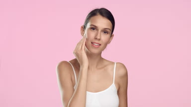 Young woman with smooth skin using cotton pad on pink background