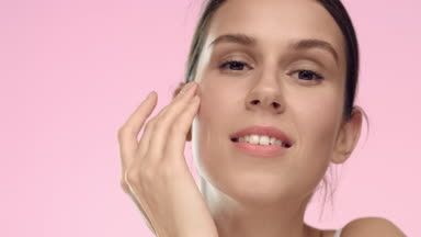 Young woman with perfect skin strokes her face and smiles.