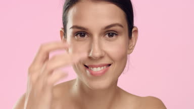 Young woman applies skincare cream on her face and smiles