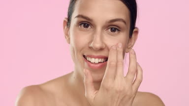 Young positive woman applies skincare cream on her face