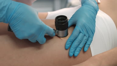 Close-up Dermatologist exams patient's skin using dermatoscope