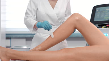 Medium shot of doctor-cosmetologist applying ipl gel on patient's leg