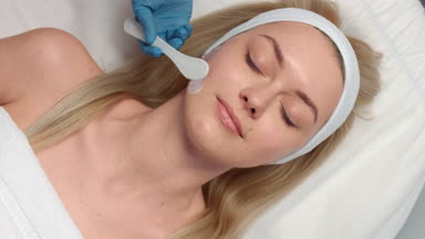 Applying cosmetology cream to patient's face using cream spatula