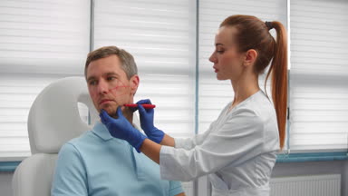 Cosmetologist draws correction lines on male patient's face