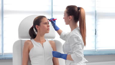 Beautician drawing correction lines on female patient's face.