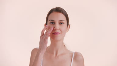 Young woman turns, looks at camera, touches her face and smiles