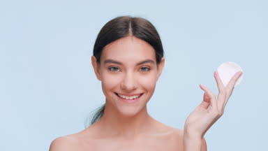 Young woman applies skin care product using a cotton pad.