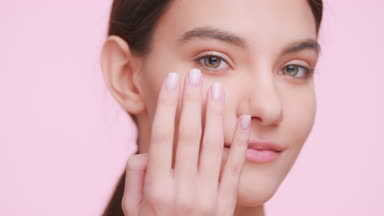 Beauty model applies cream on her face and looks at the camera