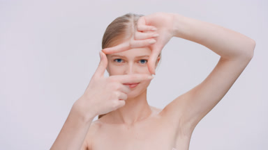 Young blonde woman looks at the camera through the finger frame