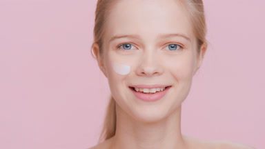 Young blonde woman applies cream on her face | Cream smear